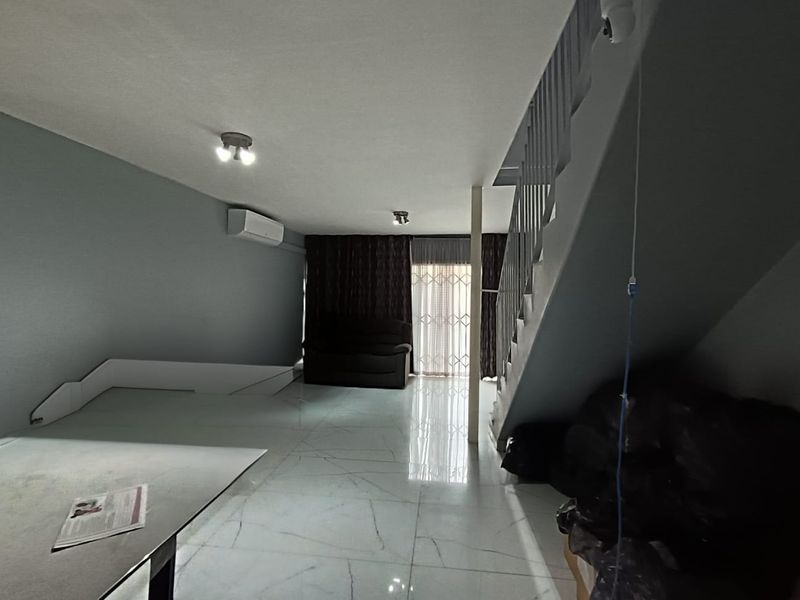 Open-plan living area featuring tiled flooring, a split-system air conditioner, and a staircase with a metal balustrade leading to the upper level.