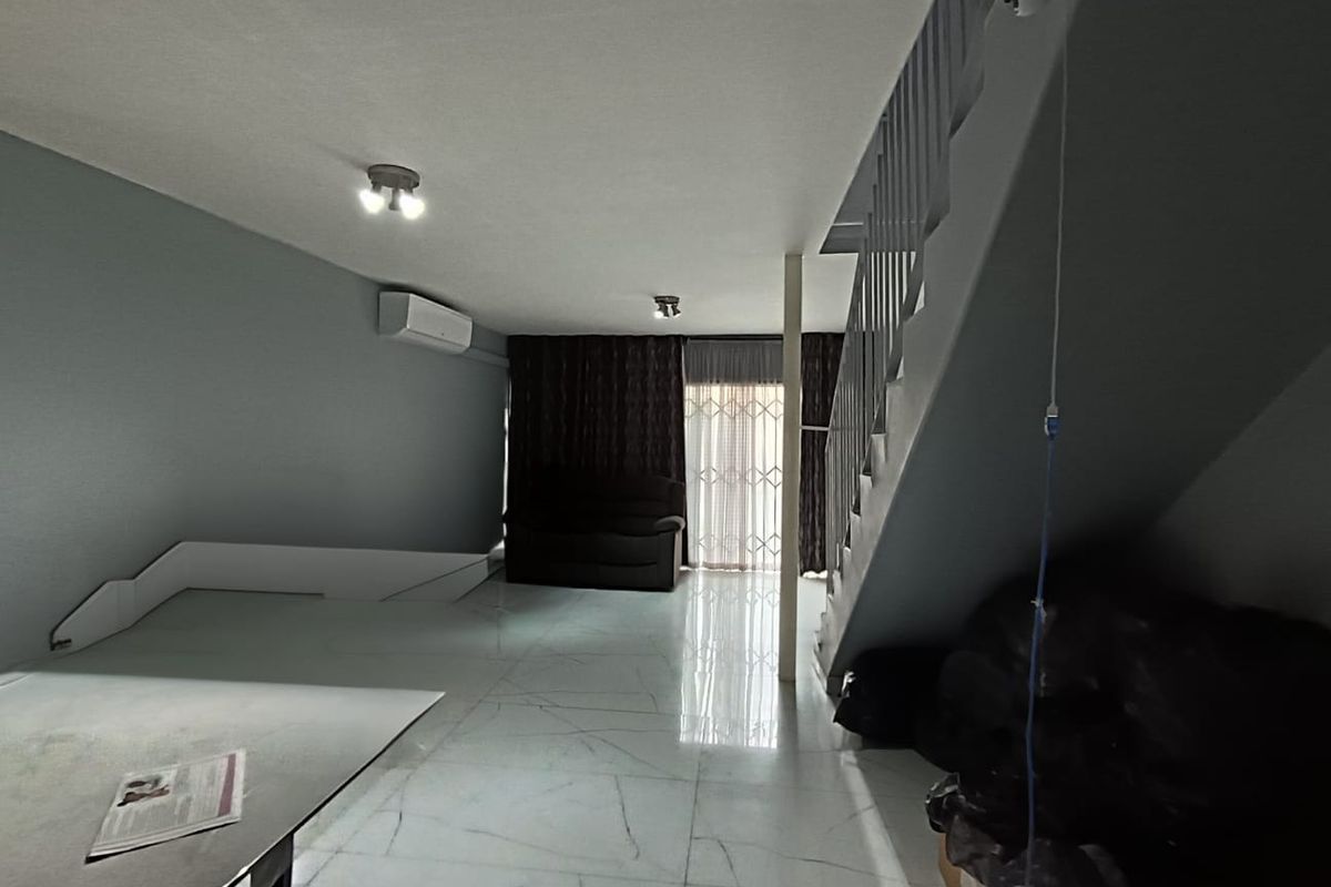 Open-plan living area featuring tiled flooring, a split-system air conditioner, and a staircase with a metal balustrade leading to the upper level.