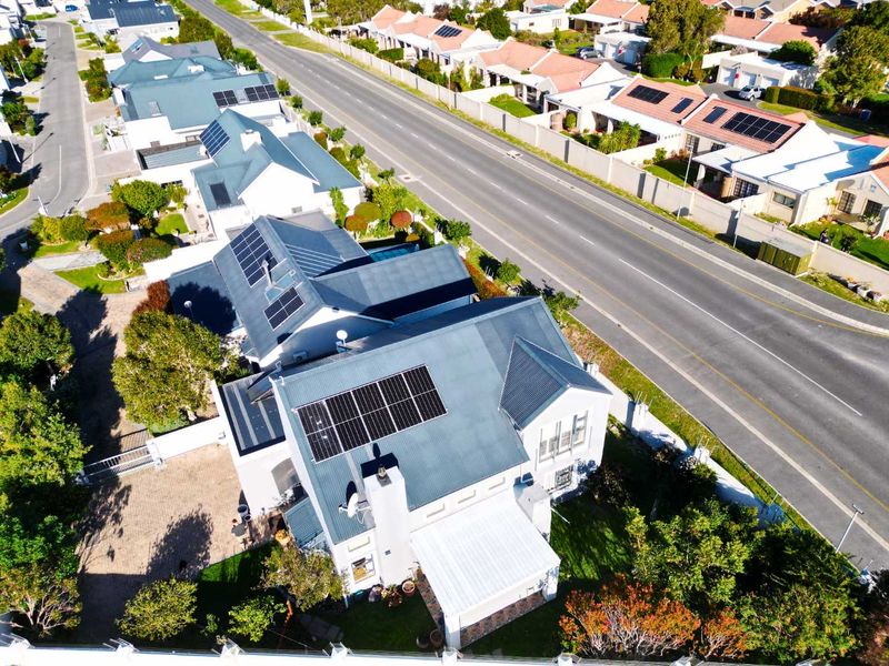 Aerial view of a residential property featuring a metal roof with installed solar panels, a paved driveway, and a well-maintained garden.