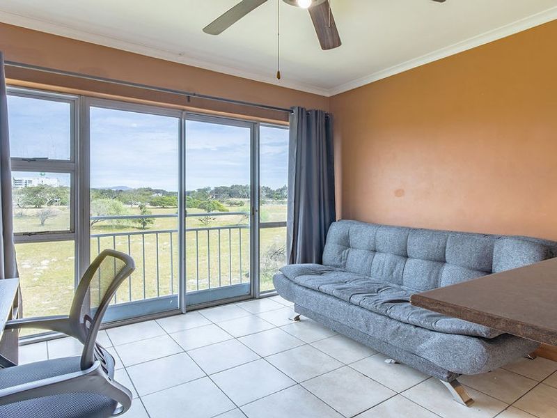 A living area featuring tiled flooring, a ceiling fan, and large sliding glass doors that open onto a balcony with scenic views.