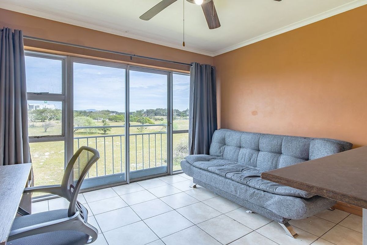 A living area featuring tiled flooring, a ceiling fan, and large sliding glass doors that open onto a balcony with scenic views.