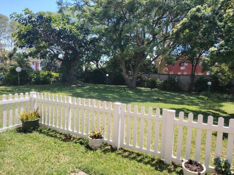 A well-maintained private garden area featuring a white picket fence, mature trees, and established lawn space.
