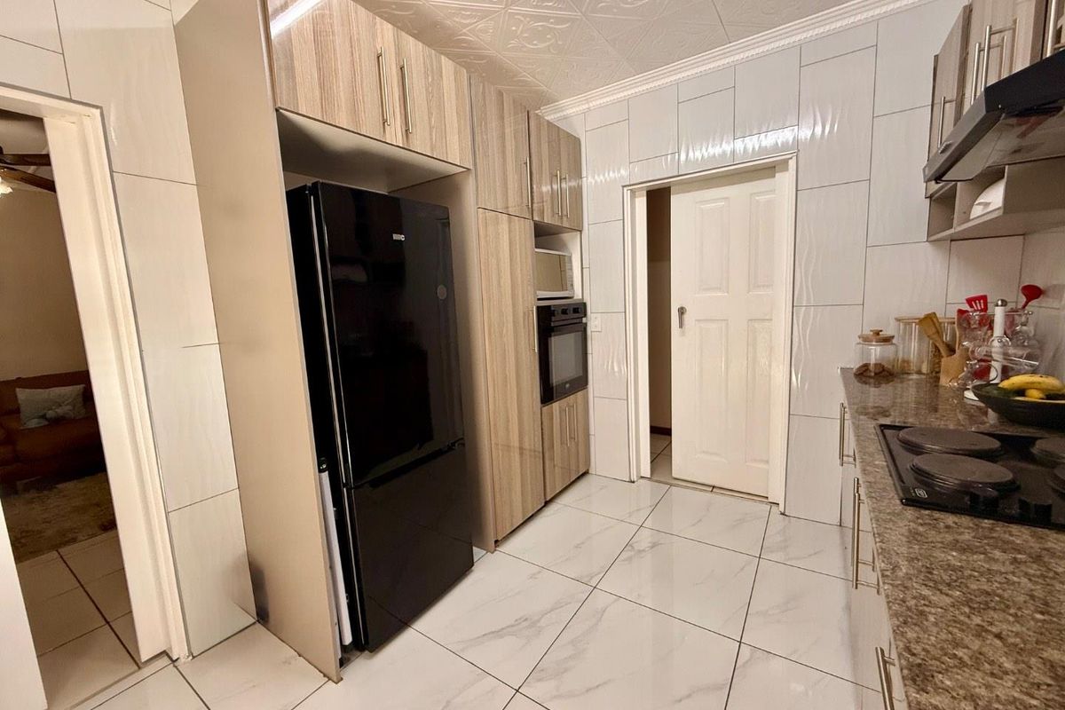 A modern kitchen featuring wood-grain cabinetry, granite countertops, a built-in oven, and tiled flooring with a decorative pressed ceiling.