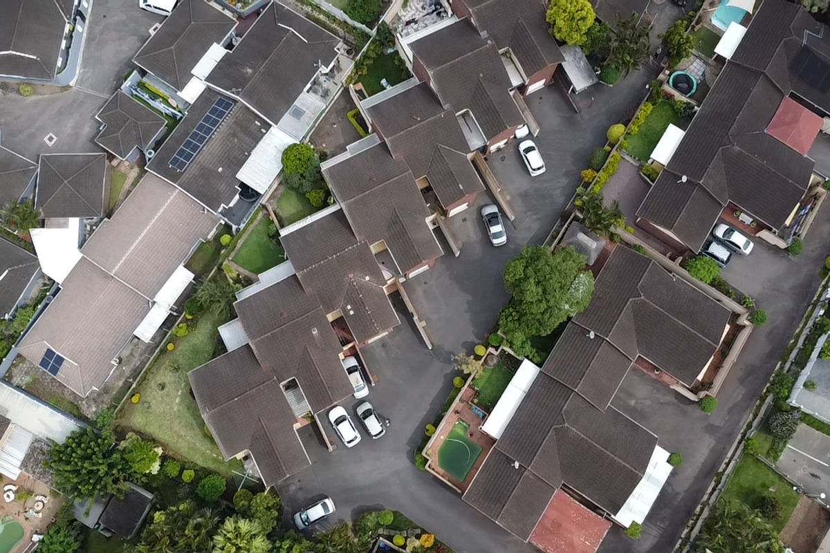 Aerial view of a townhouse complex featuring multiple residential units with tiled roofs, paved driveways, and landscaped garden areas.