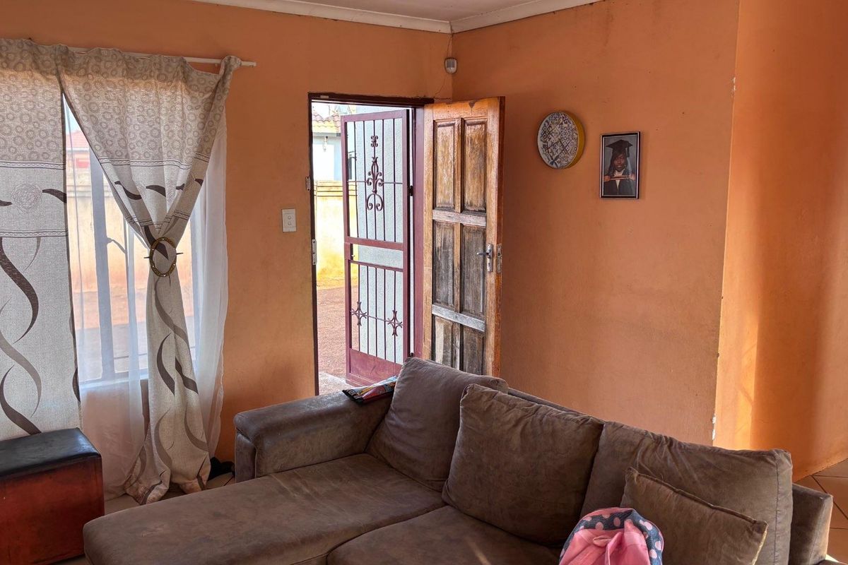 A living room area featuring tiled flooring, a security gate, and a wooden entrance door, providing direct access to the exterior.