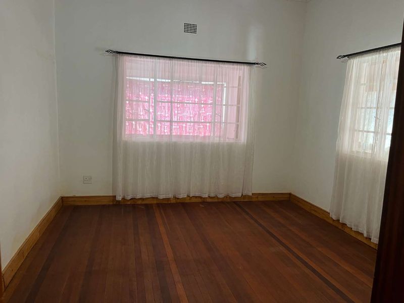 A vacant bedroom featuring polished timber flooring, timber skirting boards, and windows fitted with security bars.