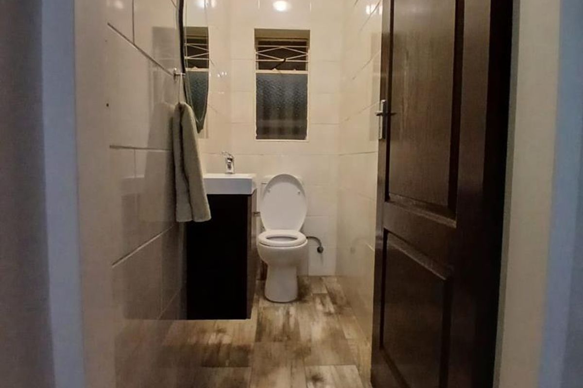 A compact, modern bathroom featuring tiled walls, wood-look floor tiles, a vanity cabinet with a washbasin, and a toilet.
