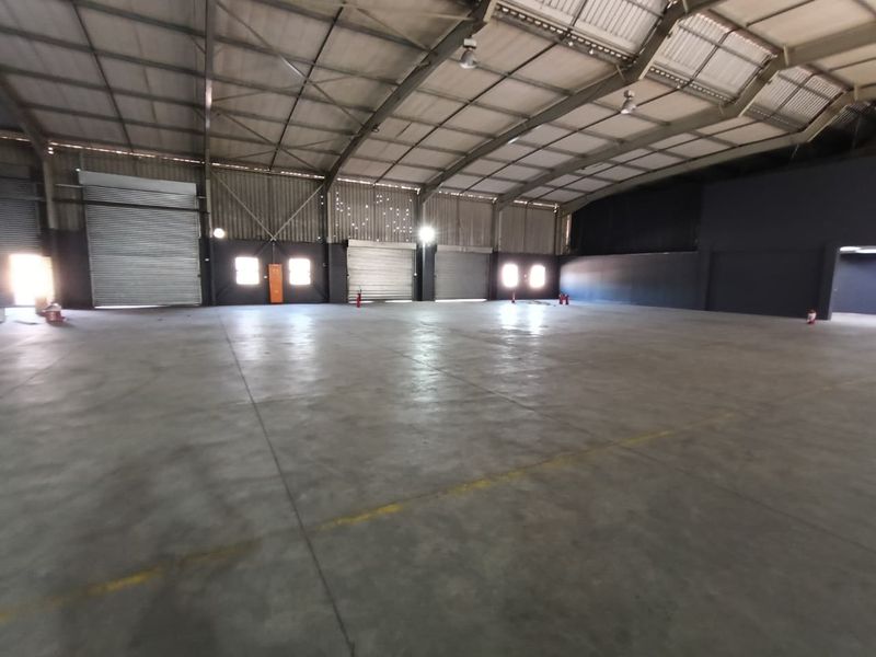 Spacious industrial warehouse featuring high ceilings with exposed steel trusses, concrete flooring, and multiple roller shutter doors for efficient access.