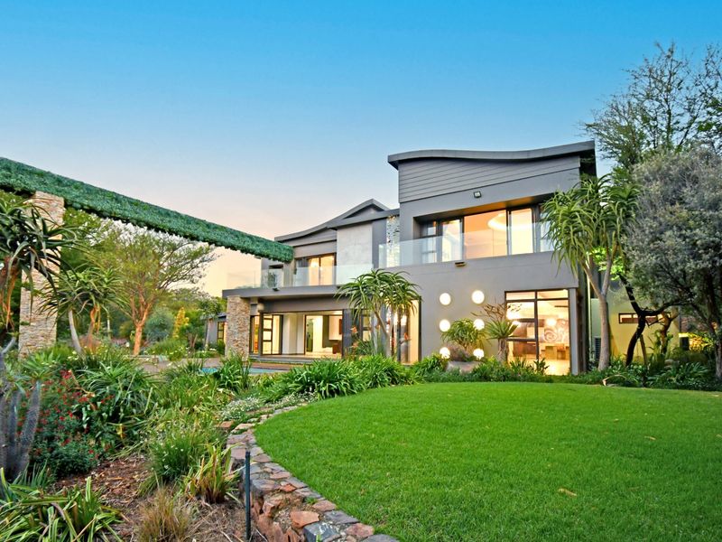 A modern double-story residence featuring contemporary architectural design, glass balustrades, stone accents, and a beautifully landscaped garden with a stone retaining wall.