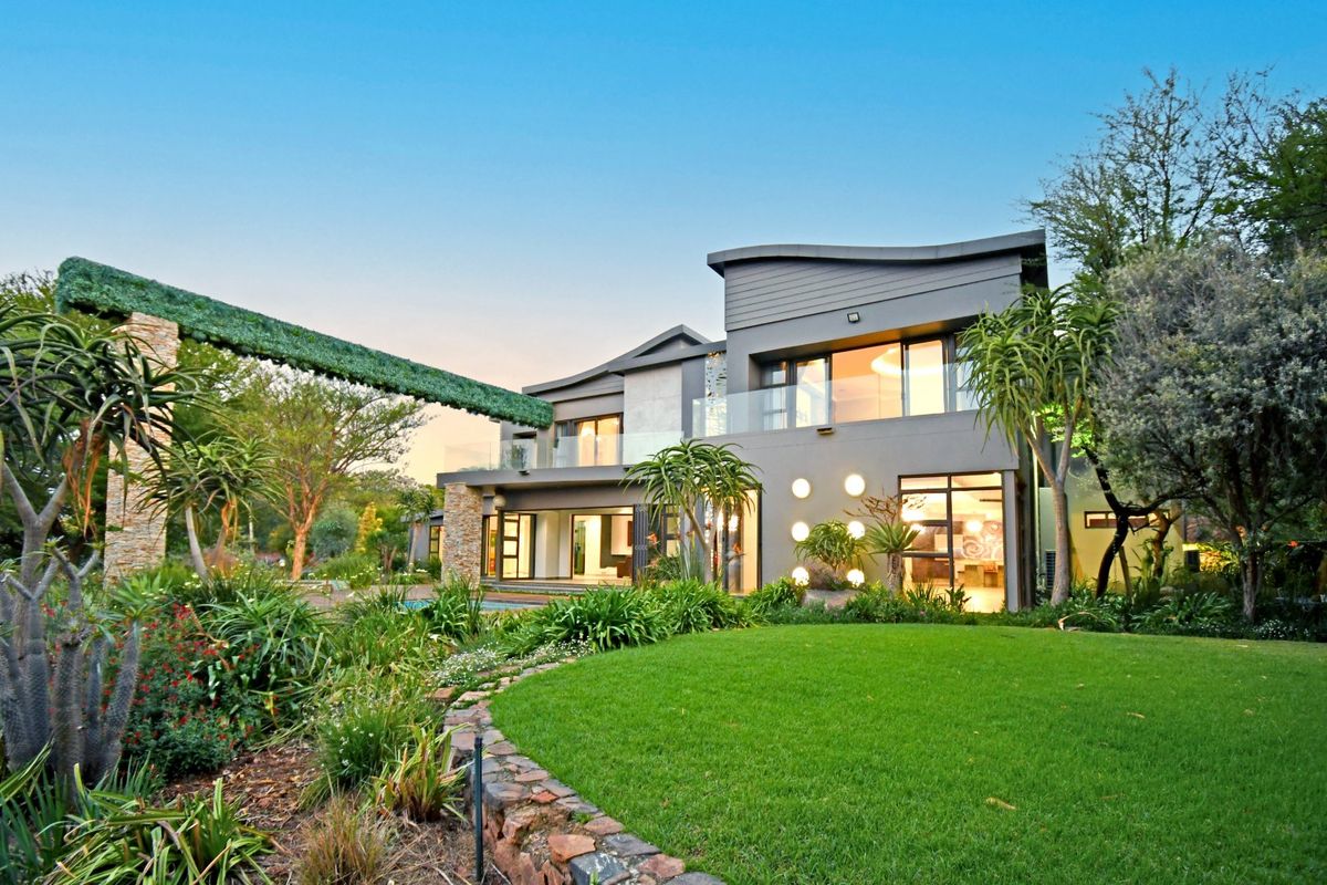 A modern double-story residence featuring contemporary architectural design, glass balustrades, stone accents, and a beautifully landscaped garden with a stone retaining wall.