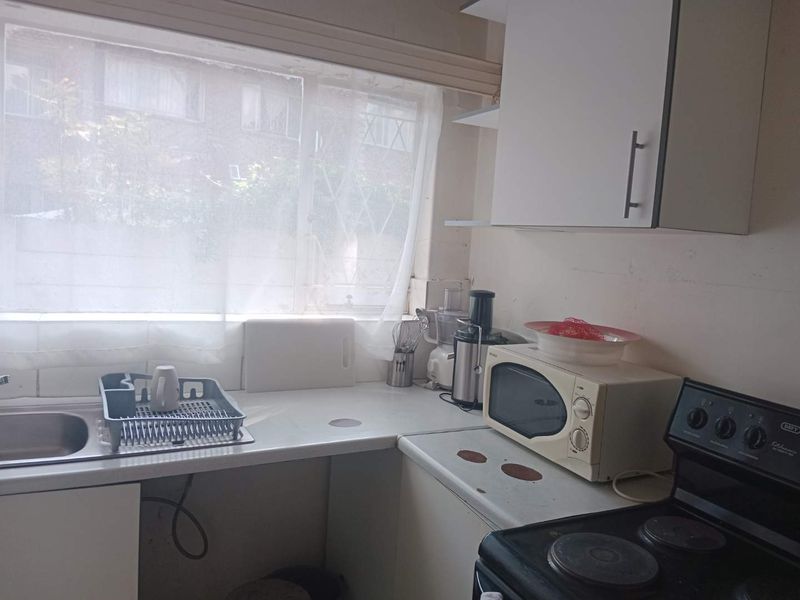 A compact kitchen featuring laminate countertops, a stainless steel sink, and built-in cabinetry, requiring cosmetic updates to modernize the space.