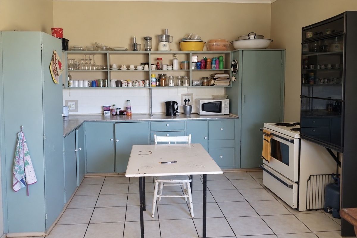 A dated kitchen featuring light blue built-in cabinetry, open shelving, tiled flooring, and a freestanding stove, offering potential for a modern renovation.
