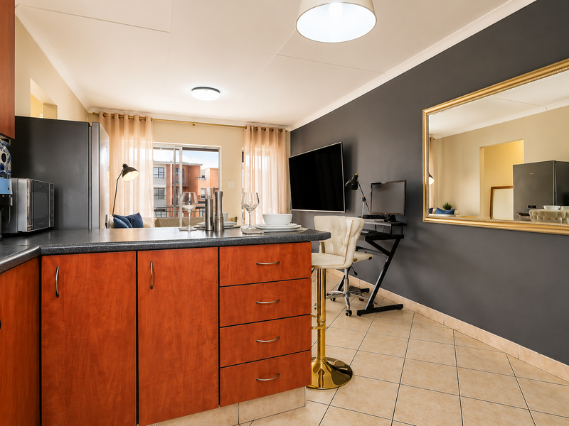 An open-plan kitchen and living area featuring wood-finish cabinetry, dark countertops, ceramic tile flooring, and a sliding door leading to an outdoor space.
