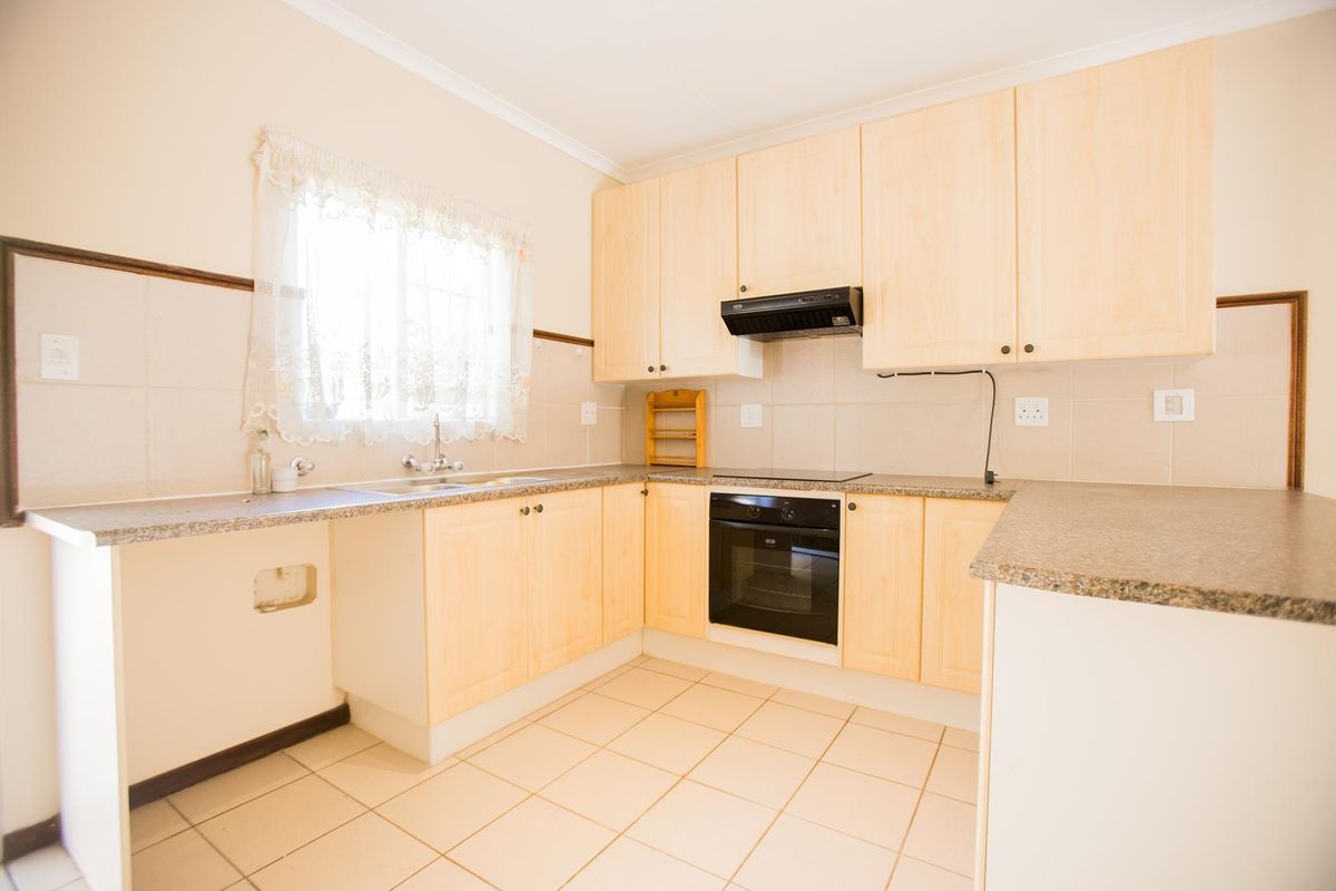 A functional kitchen featuring light wood-finish cabinetry, granite-look countertops, built-in oven, hob, extractor fan, and tiled flooring.