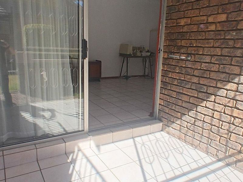 A covered patio area featuring tiled flooring and exposed brick walls, providing direct access to the interior living space through a sliding glass door.
