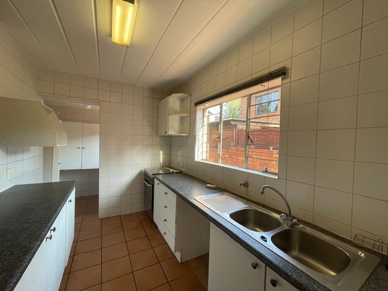 A functional, dated kitchen featuring tiled walls, laminate countertops, a double stainless steel sink, and built-in cabinetry with an adjacent scullery area.