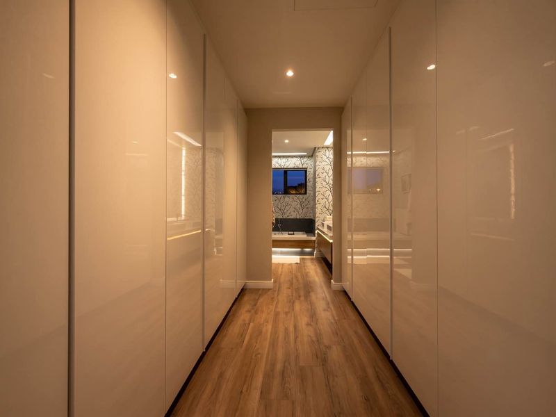 A modern, well-lit hallway featuring sleek, floor-to-ceiling built-in cabinetry and high-quality wood-look flooring, leading into a bathroom area.