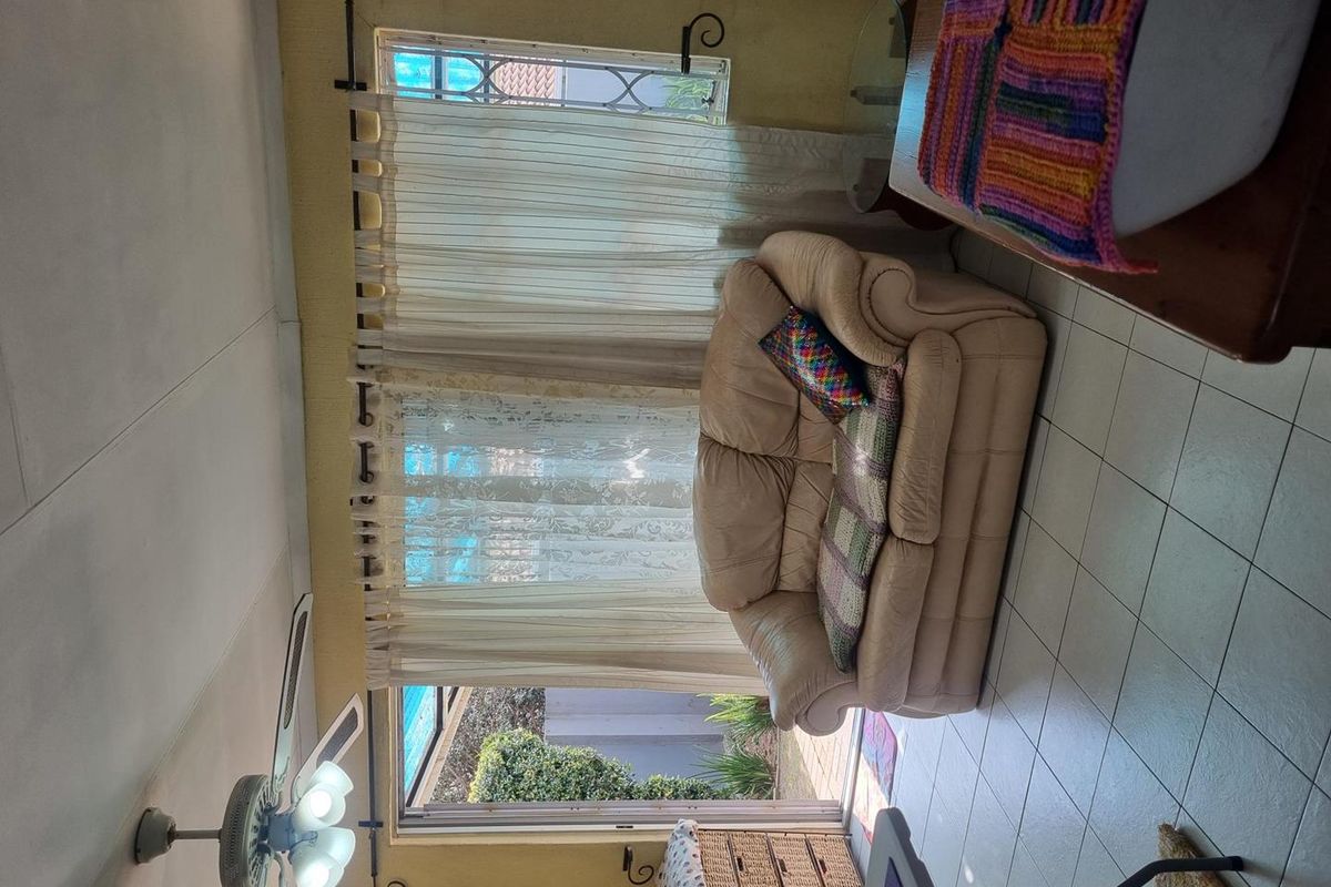 A living area featuring tiled flooring, a ceiling fan, and large windows providing natural light and access to the outdoor patio area.