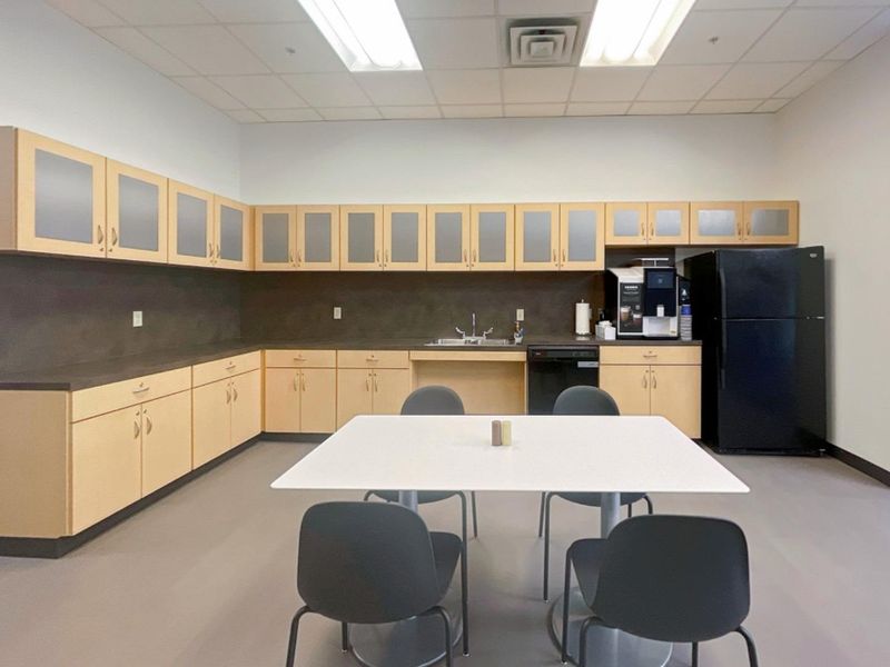 A functional office breakroom featuring extensive light wood cabinetry, laminate countertops, a stainless steel sink, and integrated dishwasher under a drop ceiling.