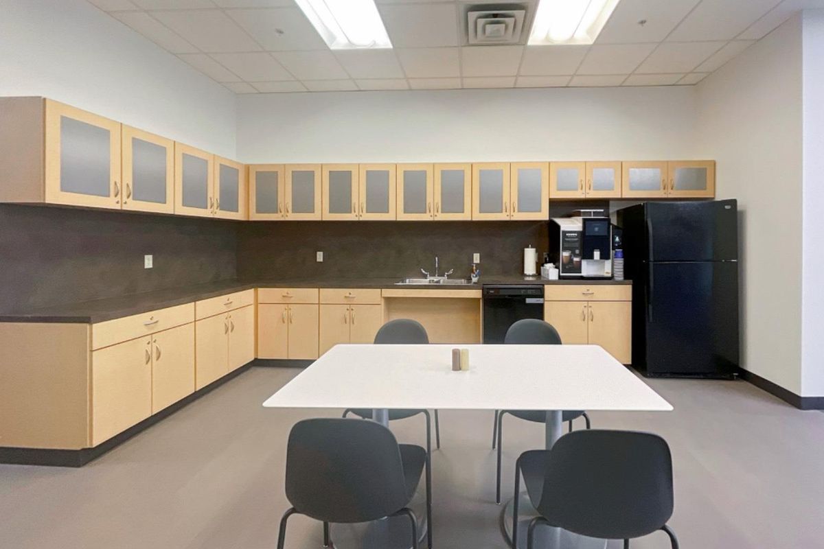 A functional office breakroom featuring extensive light wood cabinetry, laminate countertops, a stainless steel sink, and integrated dishwasher under a drop ceiling.