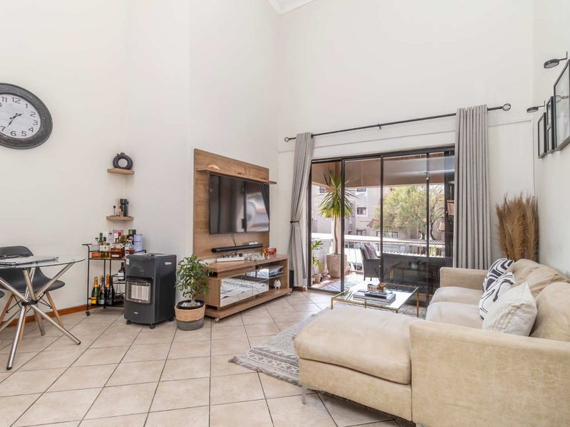 Spacious living room featuring high vaulted ceilings, tiled flooring, and large sliding glass doors that provide access to an outdoor balcony area.