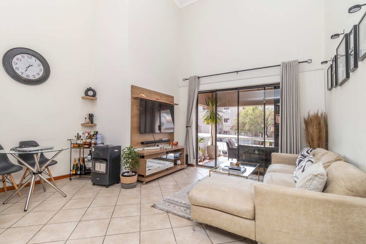 Spacious living room featuring high vaulted ceilings, tiled flooring, and large sliding glass doors that provide access to an outdoor balcony area.