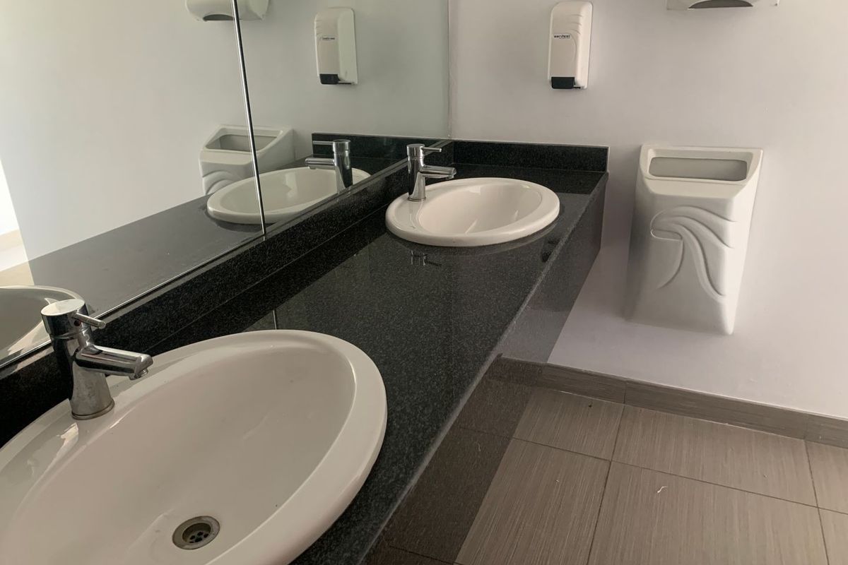 A functional office restroom featuring a dual-basin vanity with granite countertops, wall-mounted soap dispensers, and tiled flooring.