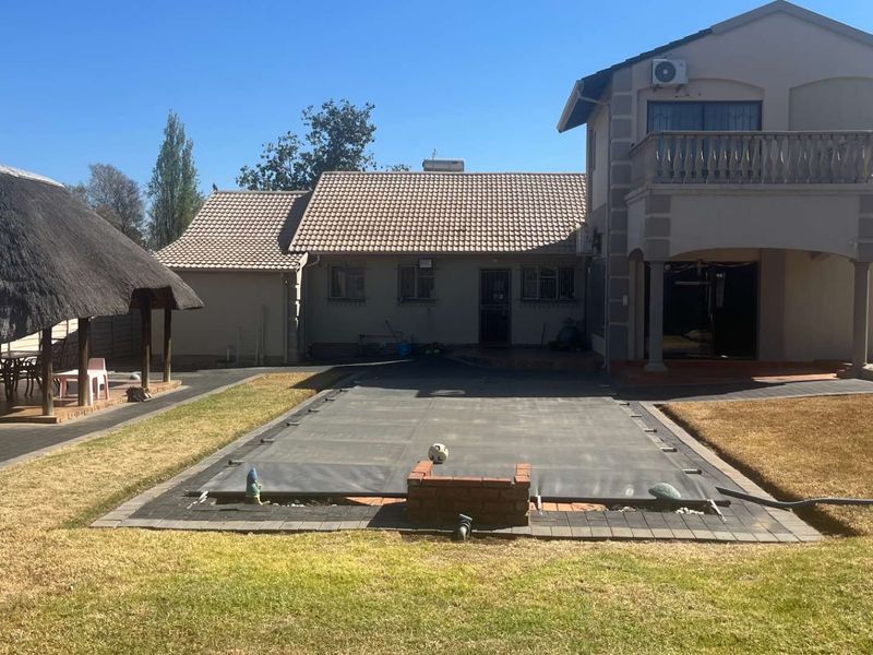 Rear view of the property featuring a swimming pool with a cover, a thatched lapa, and a two-story structure with a balcony.