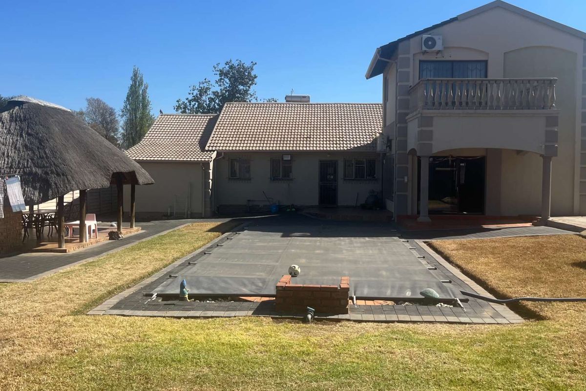 Rear view of the property featuring a swimming pool with a cover, a thatched lapa, and a two-story structure with a balcony.