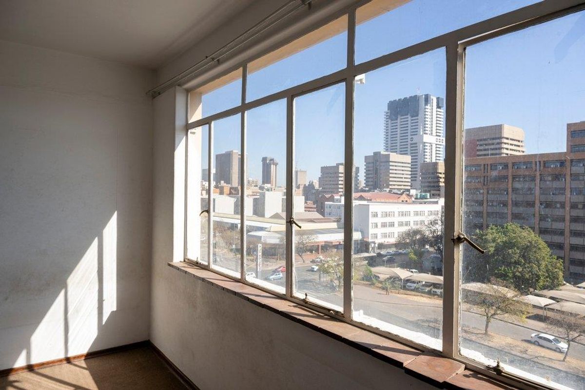 An empty room featuring large metal-framed windows that provide an expansive urban city view and natural light.