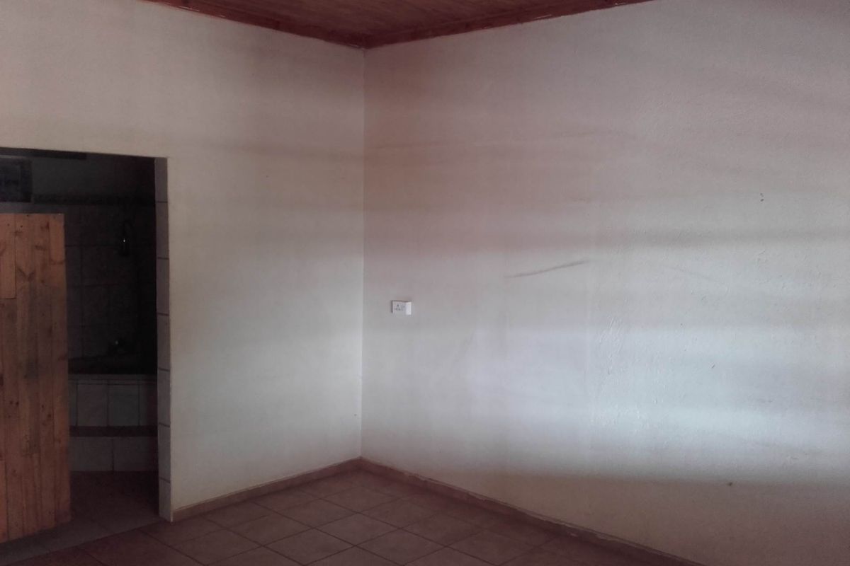 An empty interior room featuring tiled flooring, plain walls, and a timber-paneled ceiling, with an adjacent doorway leading to a secondary space.