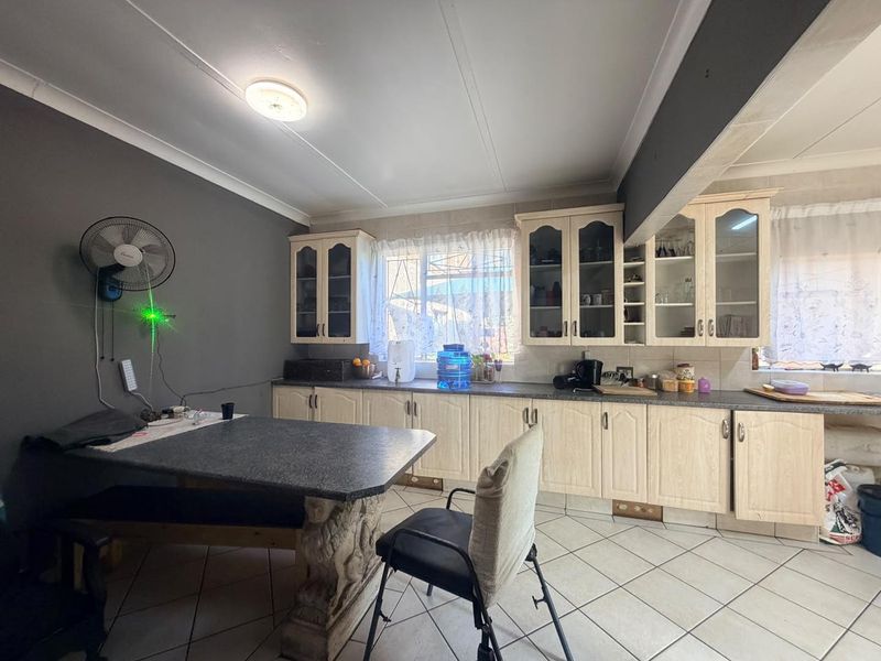 A functional kitchen featuring light-toned built-in cabinetry, glass-fronted display cupboards, laminate countertops, and tiled flooring.