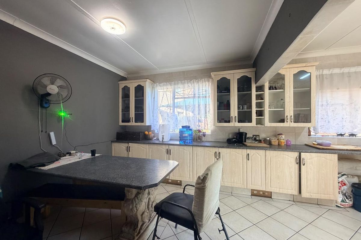 A functional kitchen featuring light-toned built-in cabinetry, glass-fronted display cupboards, laminate countertops, and tiled flooring.