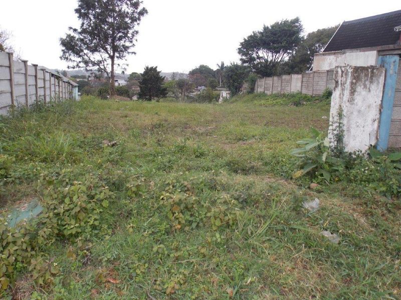 A vacant residential plot featuring overgrown grass and established precast concrete boundary walls on both sides.