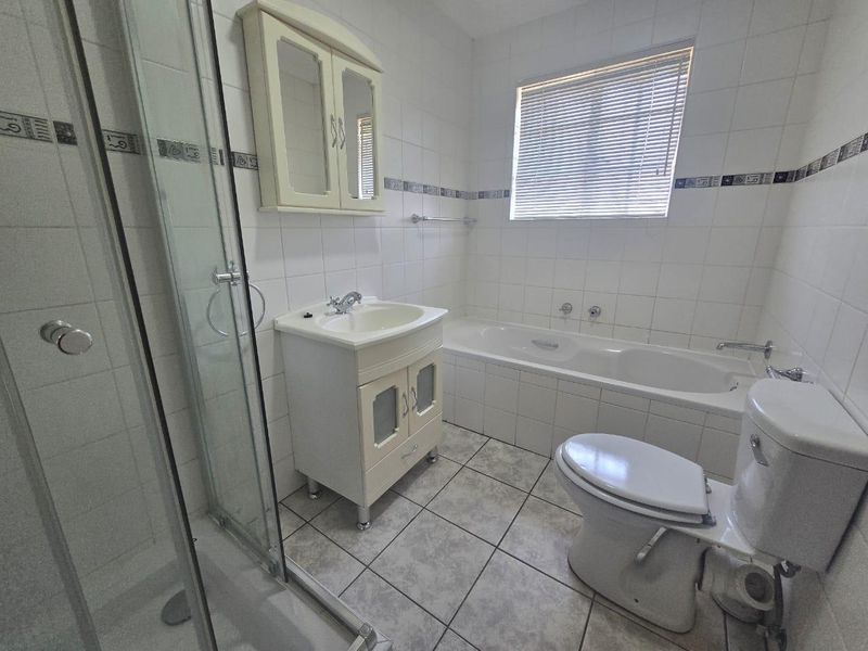 A functional bathroom featuring a separate shower enclosure, bathtub, vanity unit with basin, and wall-mounted storage cabinet with neutral tiled finishes.