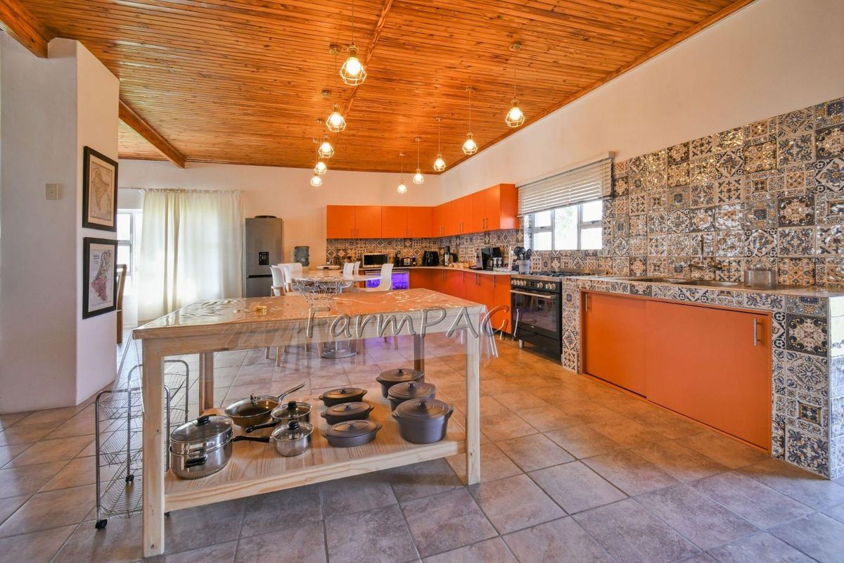 Spacious kitchen featuring vibrant orange cabinetry, decorative patterned tile backsplash, tiled flooring, and a warm timber-clad ceiling with pendant lighting.