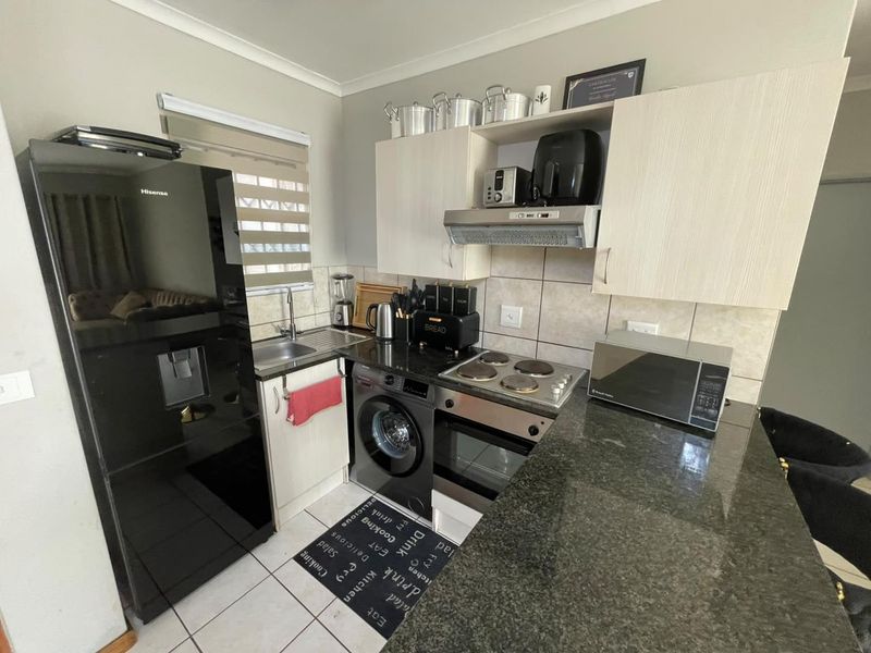 Compact kitchen featuring granite countertops, built-in oven, electric hob, extractor fan, and tiled backsplash with integrated cabinetry and sink.