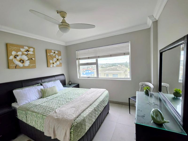 A well-maintained bedroom featuring tiled flooring, crown molding, a ceiling fan, and a window with venetian blinds offering an elevated urban view.