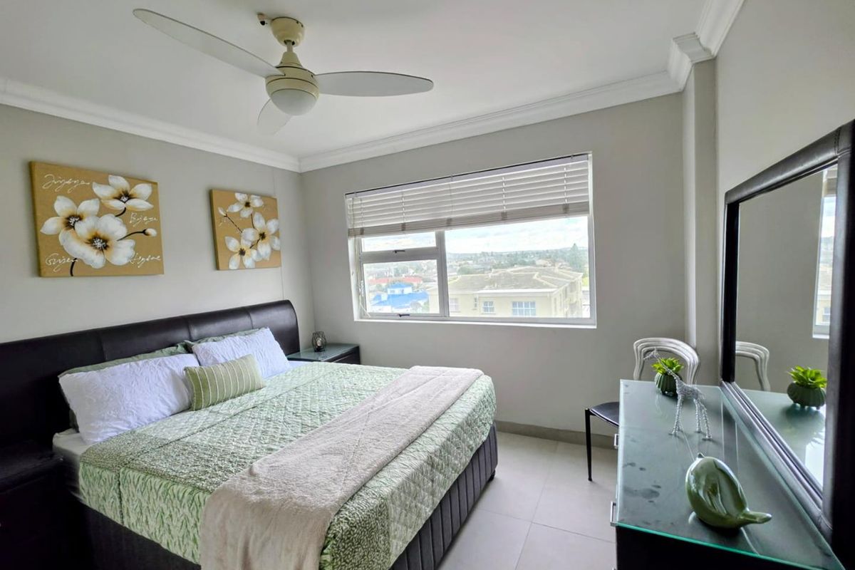 A well-maintained bedroom featuring tiled flooring, crown molding, a ceiling fan, and a window with venetian blinds offering an elevated urban view.