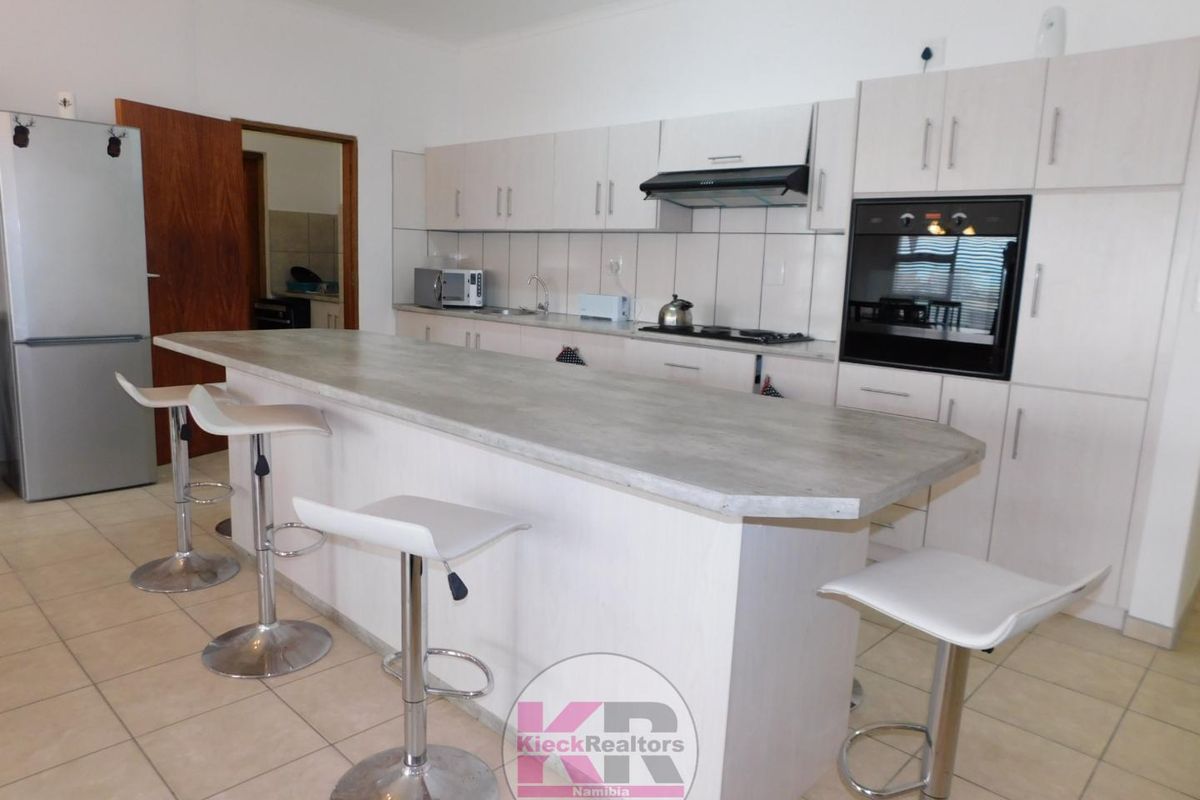 A functional kitchen featuring light-toned cabinetry, a built-in oven, extractor fan, and a central breakfast bar island with tiled flooring.