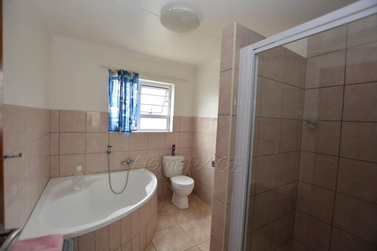A functional bathroom featuring a corner bathtub, a separate shower enclosure, and a standard toilet with neutral wall and floor tiling.