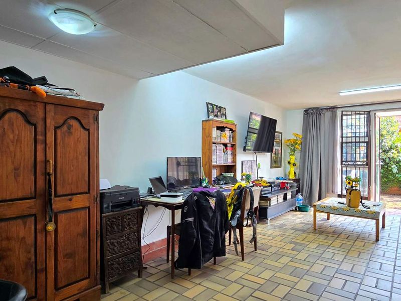 A living area featuring tiled flooring and direct access to the rear garden through a sliding door with security gate.