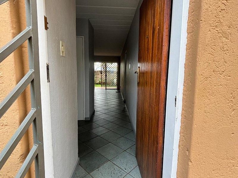 A functional hallway featuring tiled flooring, a timber entrance door, and a security gate, providing a clear transition through the townhouse.