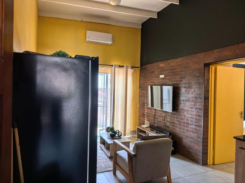 Open plan living area featuring an exposed brick wall, tiled flooring, and a split-system air conditioner with access to an outdoor balcony.