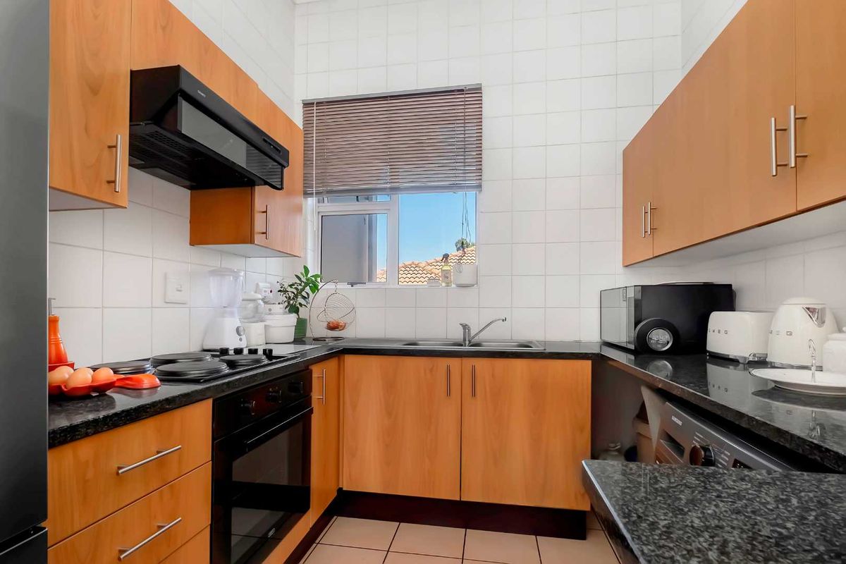 A functional kitchen featuring wood-finish cabinetry, dark granite countertops, a built-in oven, hob, extractor fan, and tiled splashbacks.