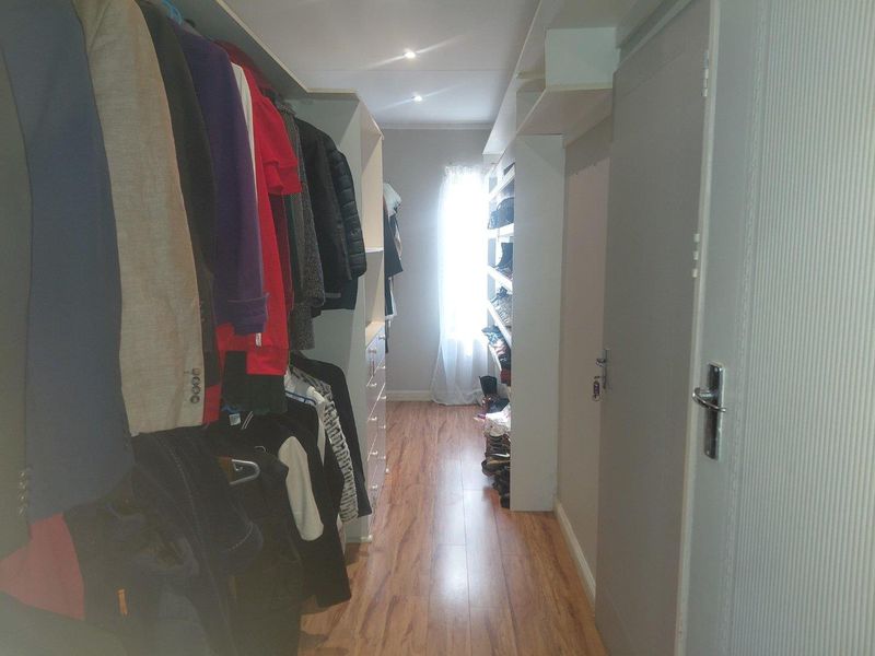 A functional walk-in closet featuring extensive built-in cabinetry, laminate flooring, and recessed lighting, providing ample storage space.