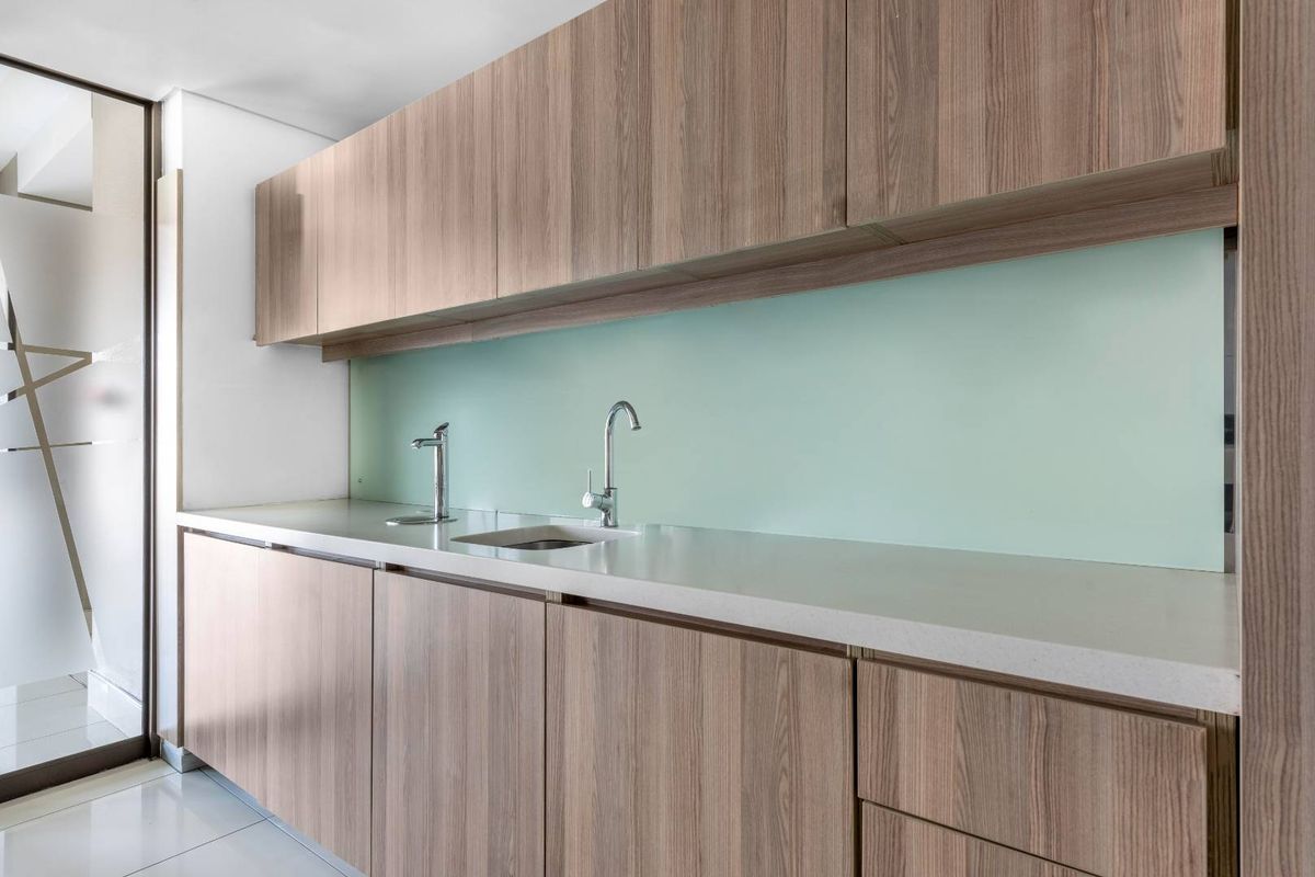 A modern office kitchenette featuring wood-grain cabinetry, a sleek stone countertop, a stainless steel sink, and a minimalist glass backsplash.