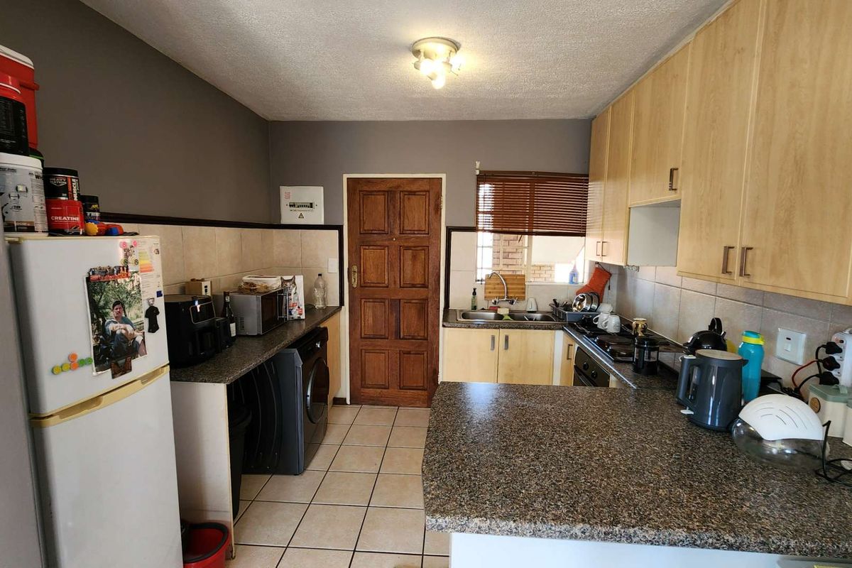 A functional kitchen featuring light wood cabinetry, granite countertops, tiled flooring, and a tiled backsplash, providing a practical workspace with integrated sink and hob.