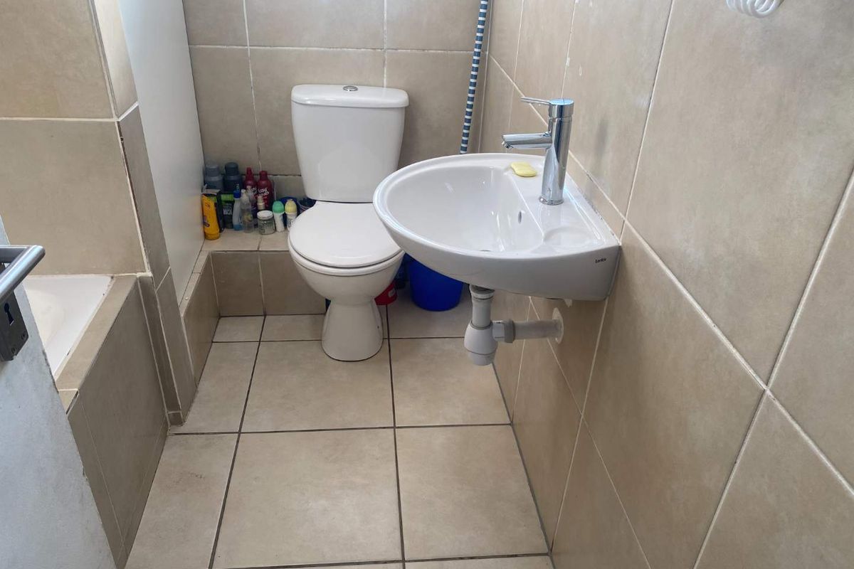 A compact bathroom featuring a wall-mounted basin, a standard toilet, and tiled walls and flooring.