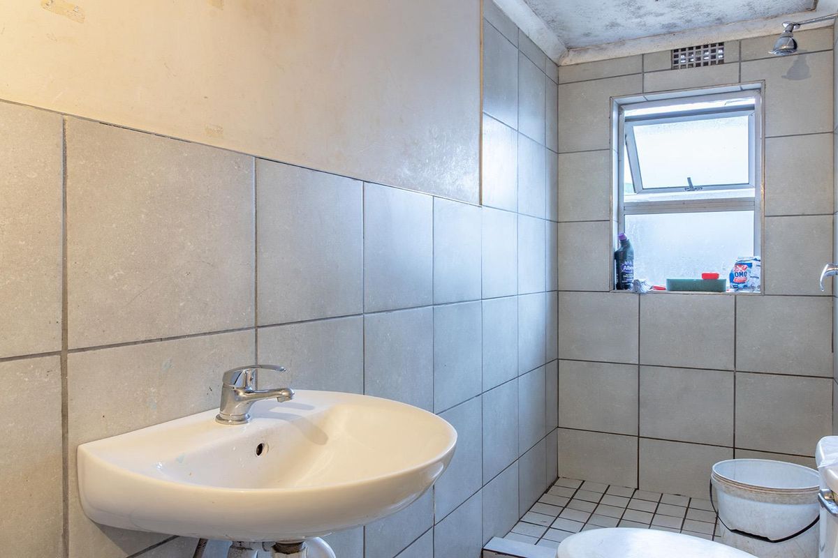 A compact bathroom featuring tiled walls and floors, a wall-mounted basin, and a shower area. The space requires cosmetic updates and ceiling repairs.